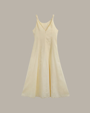 A pale cream-colored sleeveless V-neck dress with thin shoulder straps and a buttoned front, displayed against a solid taupe-gray background.