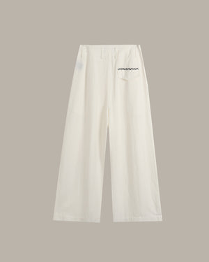 A pair of off-white wide-leg cropped pants with a small black zigzag graphic on the right hip, displayed against a solid taupe background.
