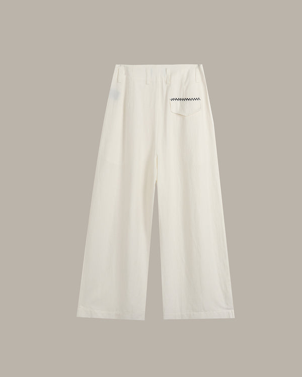 A pair of off-white wide-leg cropped pants with a small black zigzag graphic on the right hip, displayed against a solid taupe background.