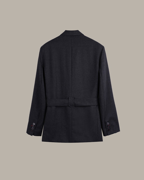 A dark navy blue belted jacket shown from the back, featuring a structured collar, long sleeves with button cuffs, and a matching waist belt, set against a solid taupe background.