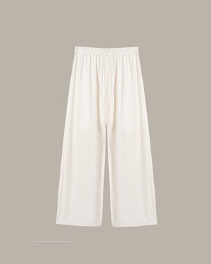 A pair of off-white wide-leg pants with an elastic waistband, displayed flat against a solid taupe background.