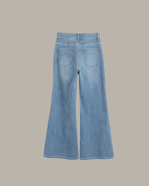 Light blue denim flare jeans shown from the back, featuring two back pockets and a wide leg silhouette, set against a solid taupe background.