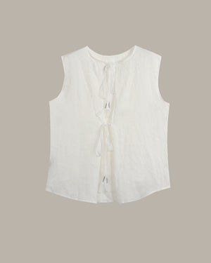 A sleeveless white top with a round neckline, front tie details, and a curved hem, shown flat against a solid taupe background.
