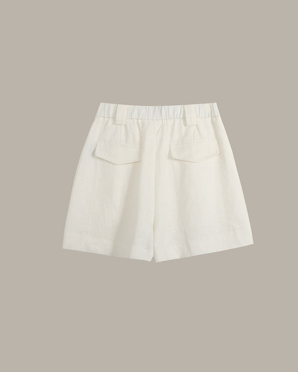 Off-white linen shorts with a pleated elastic waistband and two front patch pockets, shown flat on a solid taupe background.