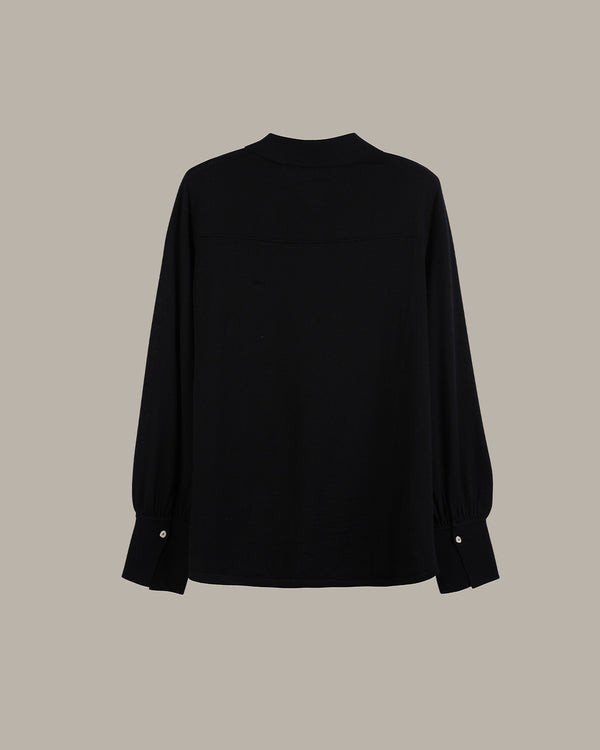 A black long-sleeve top with a mock neck and buttoned cuffs, displayed against a solid taupe background.