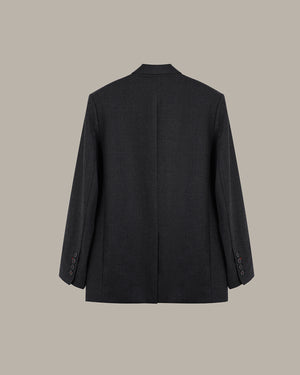 A dark charcoal gray wool blazer shown from the back, featuring a subtle textured weave and buttoned cuffs, set against a solid taupe background.