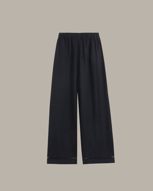 Black wide-leg cropped pants with an elastic waistband and subtle contrast stitching at the hems, shown flat against a solid taupe background.