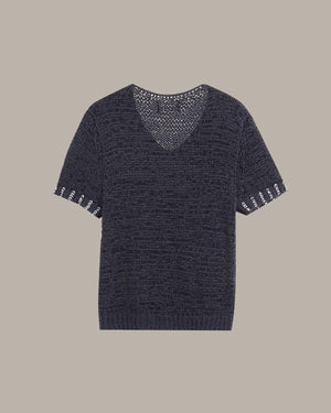 A short-sleeve knit sweater in a dark navy blue color, featuring a V-neckline with an open-knit pattern and white embroidered decorative details on the sleeve cuffs, shown against a solid taupe background.