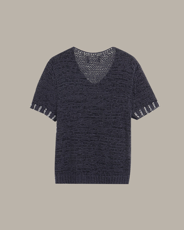 A short-sleeve knit sweater in a dark navy blue color, featuring a V-neckline with an open-knit pattern and white embroidered decorative details on the sleeve cuffs, shown against a solid taupe background.