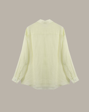 A pale yellow-green long-sleeve blouse shown from the back, featuring a high collar and buttoned cuffs, set against a solid taupe background.