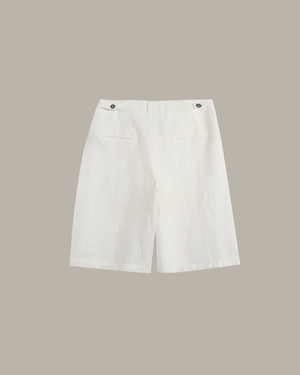 White linen shorts with a relaxed fit, featuring two buttoned flap pockets on the back, displayed against a solid taupe background.