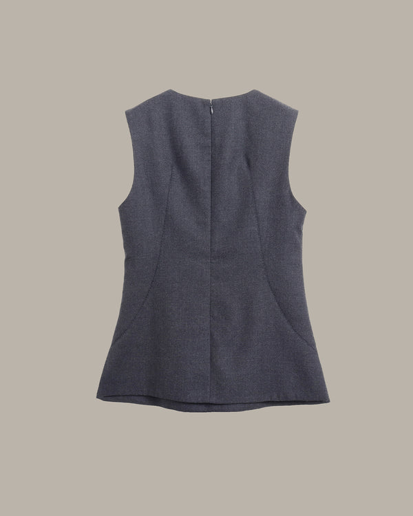 A sleeveless dark slate blue top shown from the back, featuring a central seam and a small metal ring detail at the neckline, set against a solid taupe background.