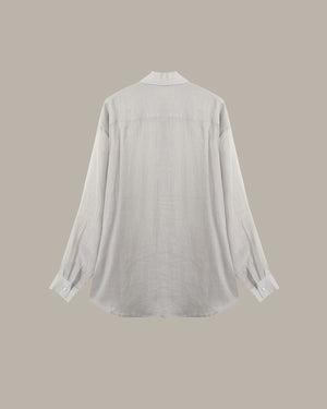 A light gray long-sleeve linen shirt shown from the back, featuring a relaxed fit, buttoned cuffs, and a simple collar, set against a solid taupe background.