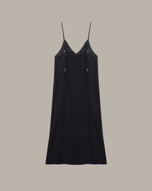 A black spaghetti-strap slip dress with a V-neckline and small silver-tone decorative accents on the chest, shown against a solid taupe background.