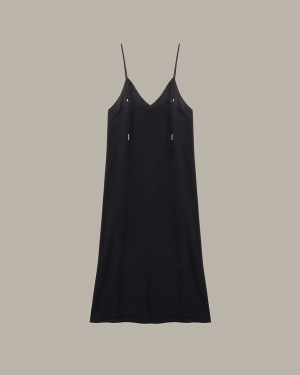 A black spaghetti-strap slip dress with a V-neckline and small silver-tone decorative accents on the chest, shown against a solid taupe background.