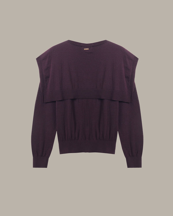 A dark plum purple knit sweater with a layered, asymmetrical ruffle design across the chest and long sleeves, shown flat against a solid taupe background.