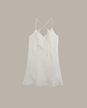 A white cotton camisole top with thin adjustable spaghetti straps and a drawstring tie at the V-neck, shown against a solid taupe background.