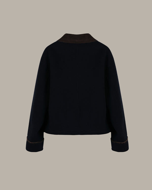 A dark navy blue cropped jacket with contrasting brown collar and cuff trim, shown from the back against a solid taupe background.