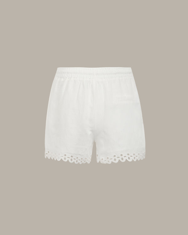 White cotton eyelet shorts with a scalloped eyelet hem and an elastic waistband, shown flat on a solid taupe background.