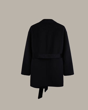 A black wrap coat with a self-tie belt, shown from the back against a solid taupe background.