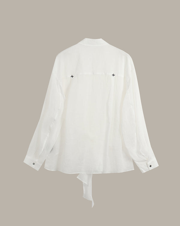 A white long-sleeve shirt shown from the back, featuring a relaxed fit, buttoned cuffs, and a tie detail at the bottom hem, set against a solid taupe background.