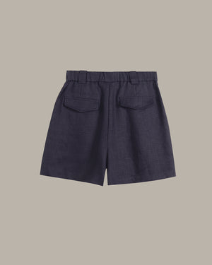 Dark navy blue shorts with a pleated waistband and two back patch pockets, shown flat against a solid taupe background.
