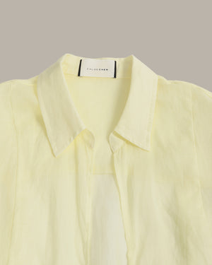 A pale yellow long-sleeve button-up shirt with a pointed collar, shown in a close-up studio shot against a solid taupe background. The brand label 'CLOTHING' is visible inside the collar.