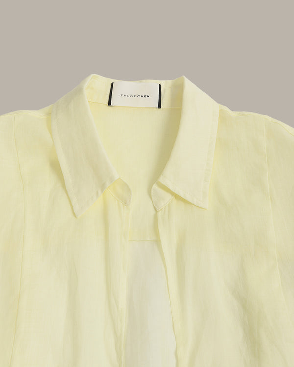 A pale yellow long-sleeve button-up shirt with a pointed collar, shown in a close-up studio shot against a solid taupe background. The brand label 'CLOTHING' is visible inside the collar.