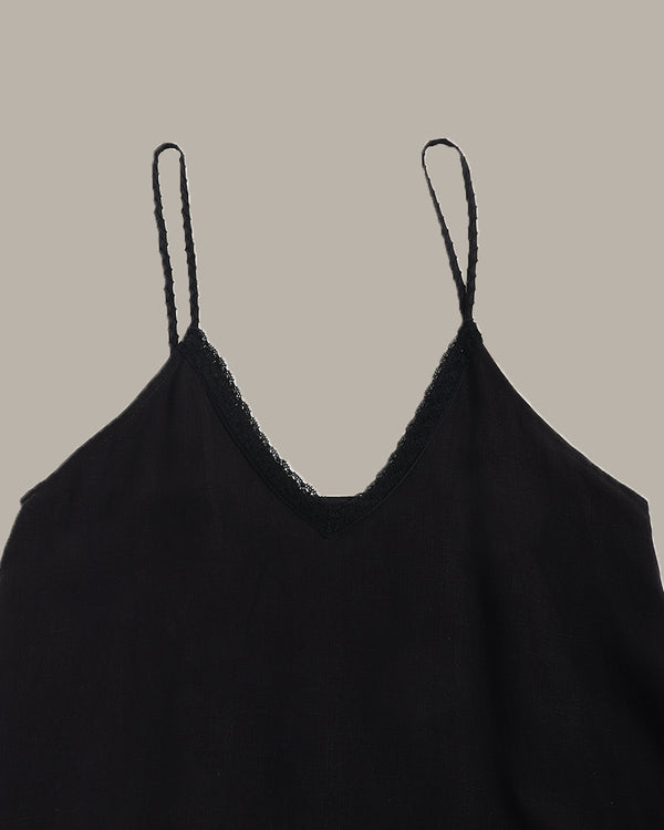 A close-up of a black spaghetti-strap camisole top with a delicate lace trim along the V-neckline, shown against a solid taupe background.