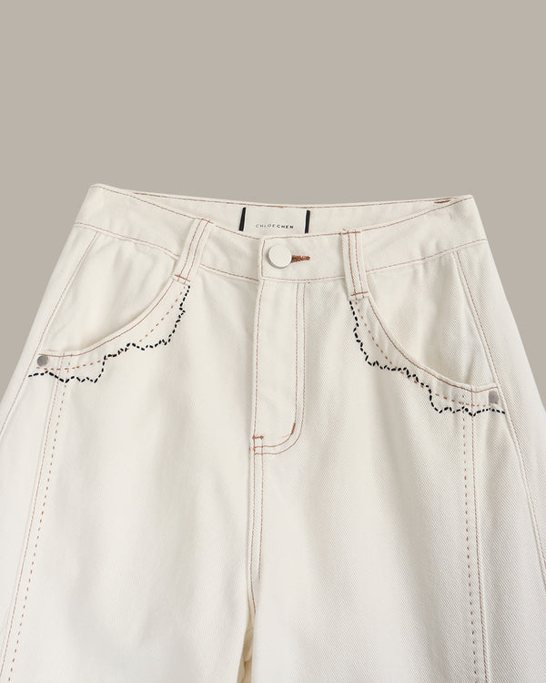 Close-up of light-colored jeans with decorative stitching on a neutral background