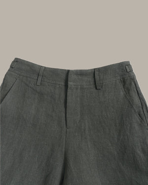 Close-up of the waistband and upper front of dark gray trousers, showing belt loops, front fly, and side pockets against a plain warm beige background.