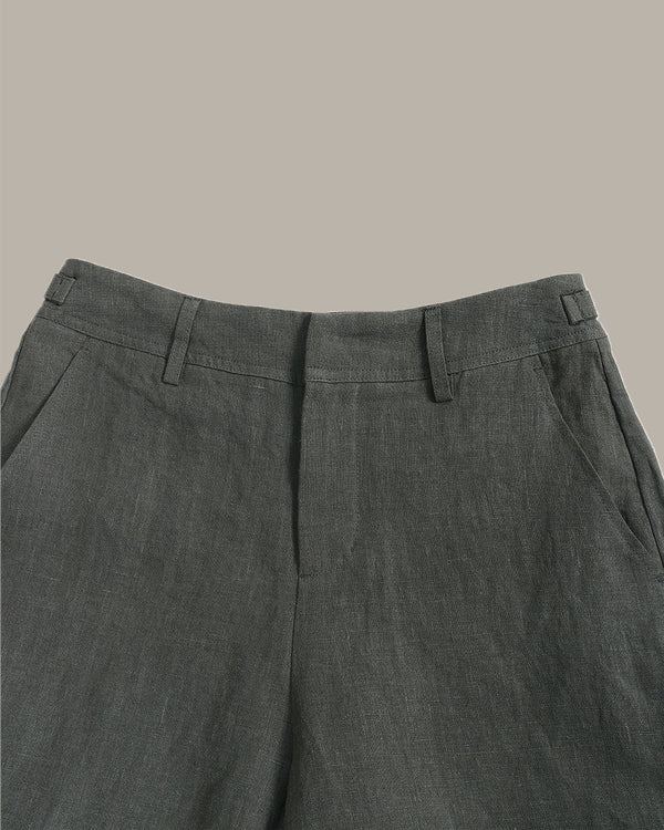 Close-up of the waistband and upper front of dark gray trousers, showing belt loops, front fly, and side pockets against a plain warm beige background.