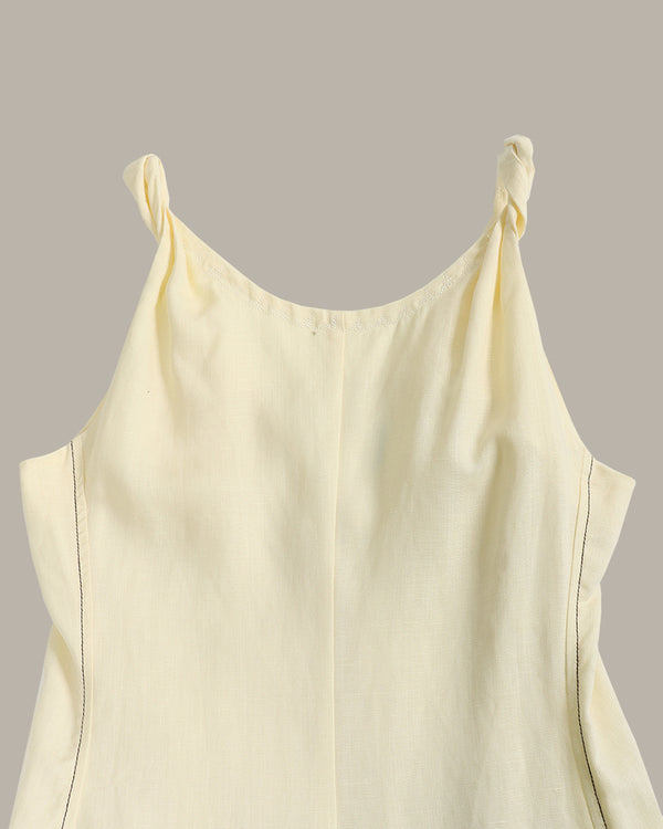A close-up of a pale cream or off-white sleeveless top with twisted shoulder straps, shown against a solid taupe-gray background.
