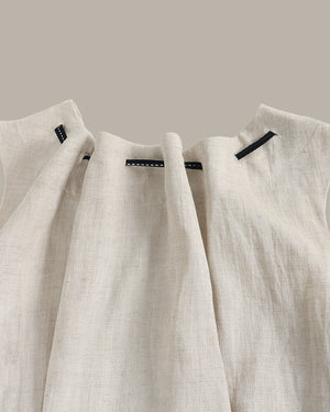 Two beige linen shirts hanging on a rack against a neutral background