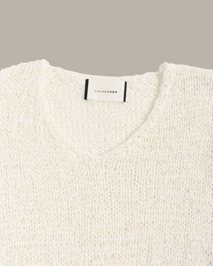 Close-up of a textured cream knit sweater with a V-neck collar, featuring a white neck label with black text that reads 'CHLOE CHEN'.