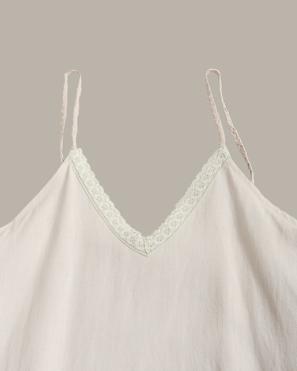 A close-up of a light cream or off-white camisole top with thin spaghetti straps and a delicate floral lace trim along the V-neckline, set against a solid taupe background.