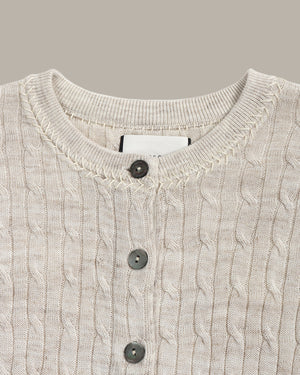 Close-up of a cable knit cardigan with button details on a neutral background
