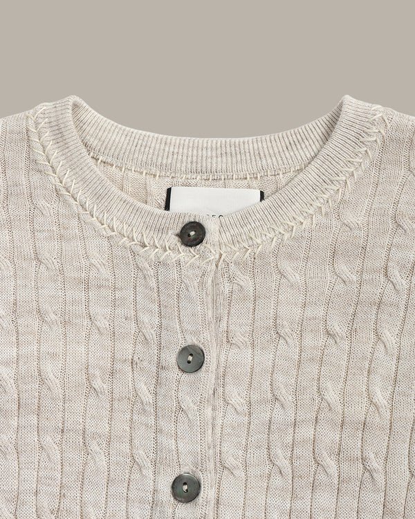Close-up of a cable knit cardigan with button details on a neutral background