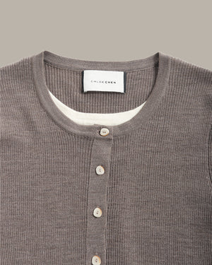 Close-up of a ribbed knit Henley shirt by Chloé Ché, in a taupe-brown color, featuring a white inner collar and light-colored buttons.