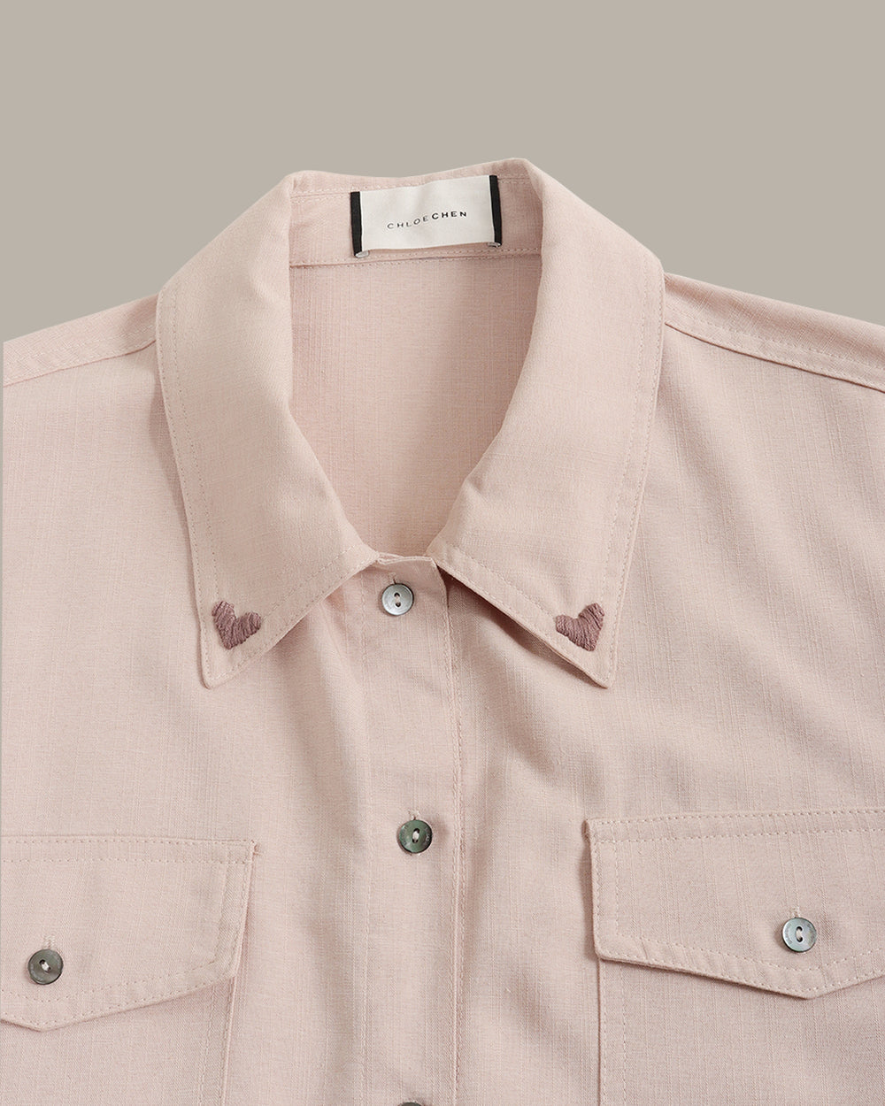 Pink jacket with button details, heart embroidery on collars on a beige background