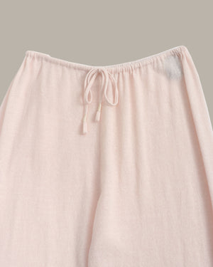 Close-up of a light blush pink drawstring lounge pant leg, showing the soft textured fabric and elastic waistband against a solid neutral background.