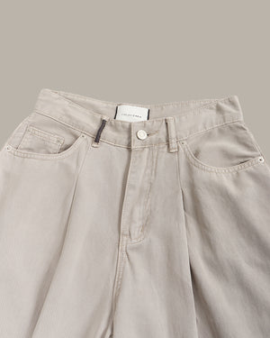 Close-up of a pair of light beige wide-leg denim pants, showing the waistband, button closure, belt loops, and front pockets against a solid taupe background.