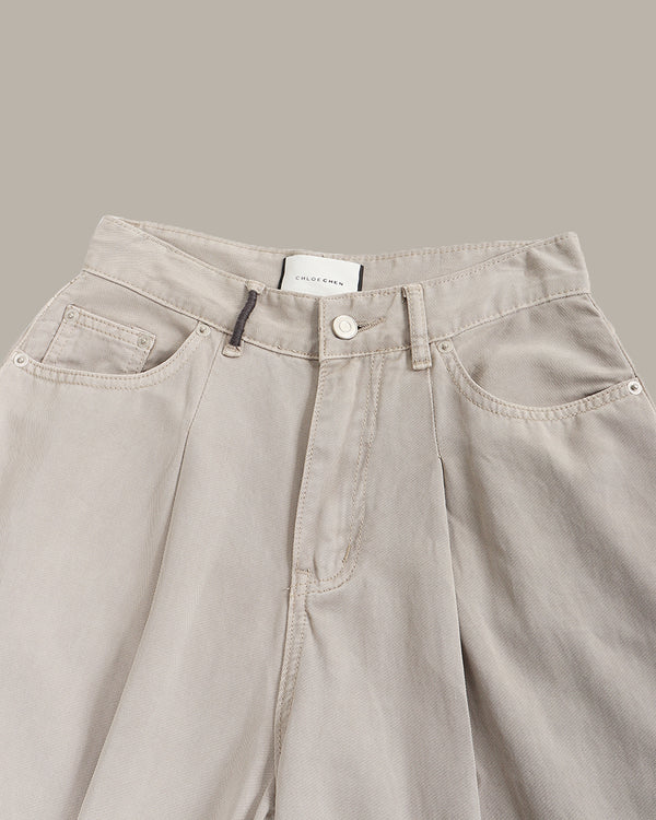 Close-up of a pair of light beige wide-leg denim pants, showing the waistband, button closure, belt loops, and front pockets against a solid taupe background.