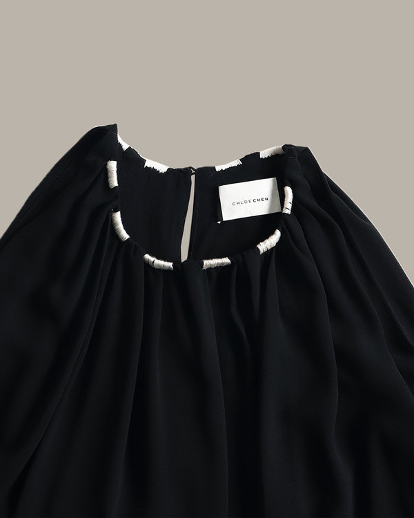 Close-up of a black top with a gathered neckline and white embroidered trim details, featuring a visible 'MILITHEMEN' brand label.