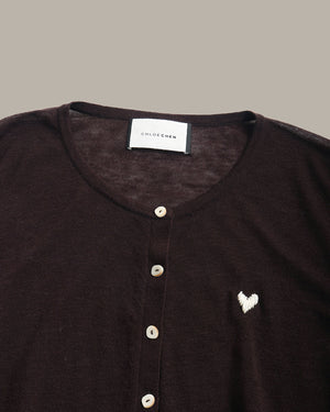 Close-up of a dark brown knit henley top by Chloe Chen, featuring a white embroidered heart on the chest and a white brand label at the collar.
