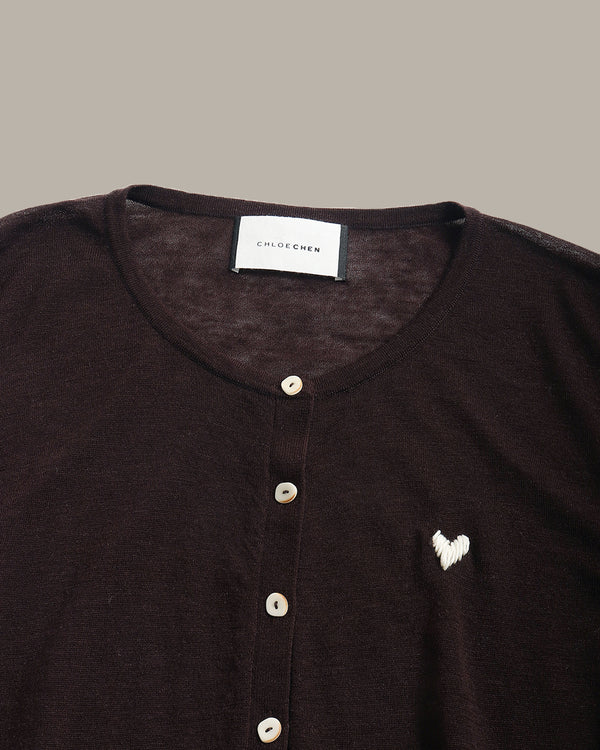 Close-up of a dark brown knit henley top by Chloe Chen, featuring a white embroidered heart on the chest and a white brand label at the collar.