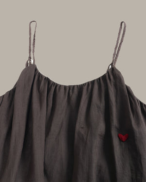 Dark gray dress with thin straps and a red heart detail on a beige background