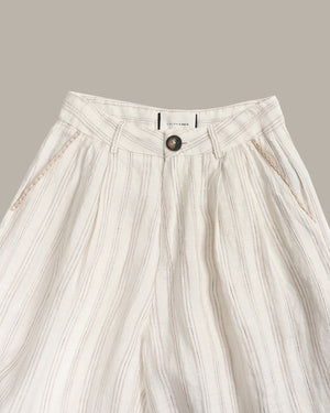 Close-up of a pair of high-waisted, wide-leg trousers in a cream-colored linen-like fabric with vertical stripes and a single dark button closure at the front waistband.