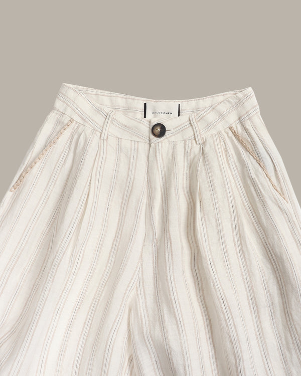 Close-up of a pair of high-waisted, wide-leg trousers in a cream-colored linen-like fabric with vertical stripes and a single dark button closure at the front waistband.