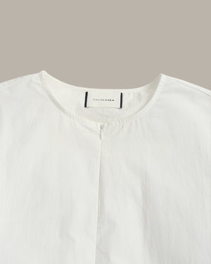 Close-up of a white button-front top with a round neckline and a visible neck label reading 'COLORFEDEN' against a plain taupe background.
